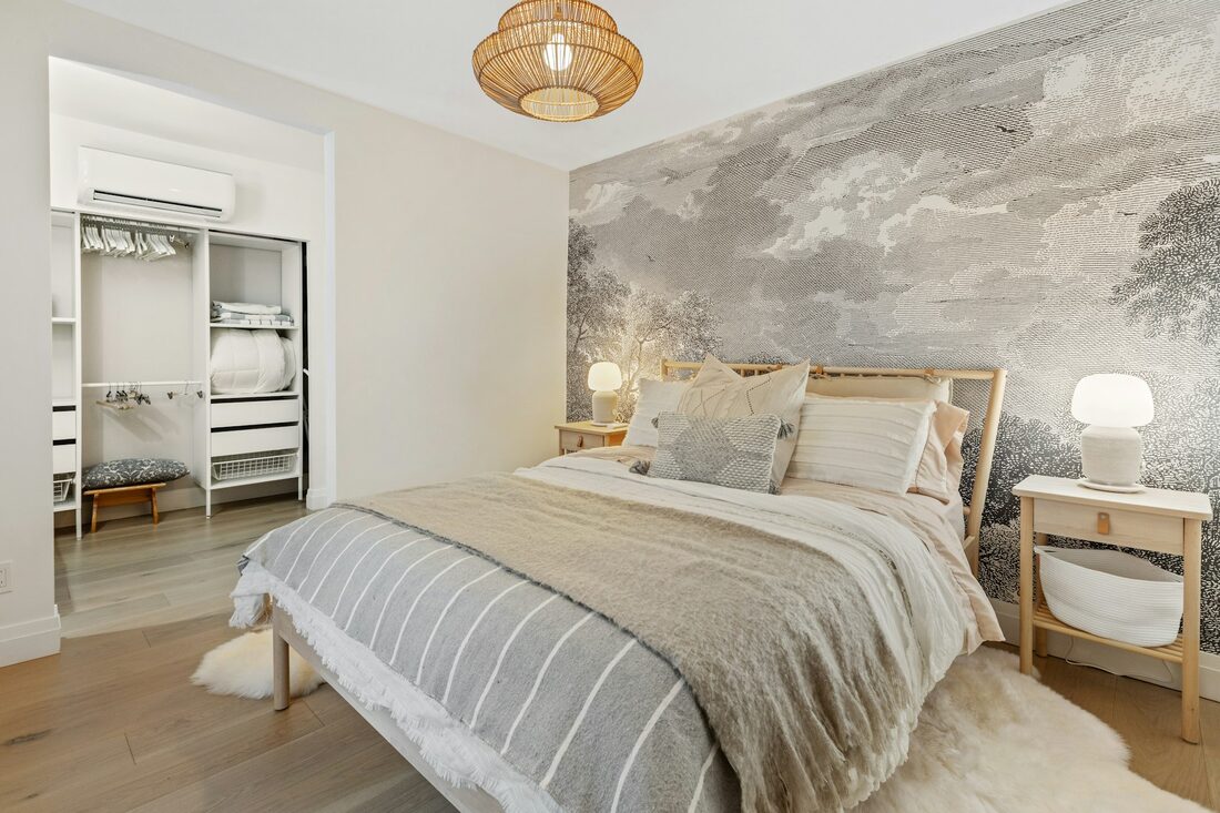 Bedroom with a soft grey landscape mural wallpaper behind the bed and a woven pendant light