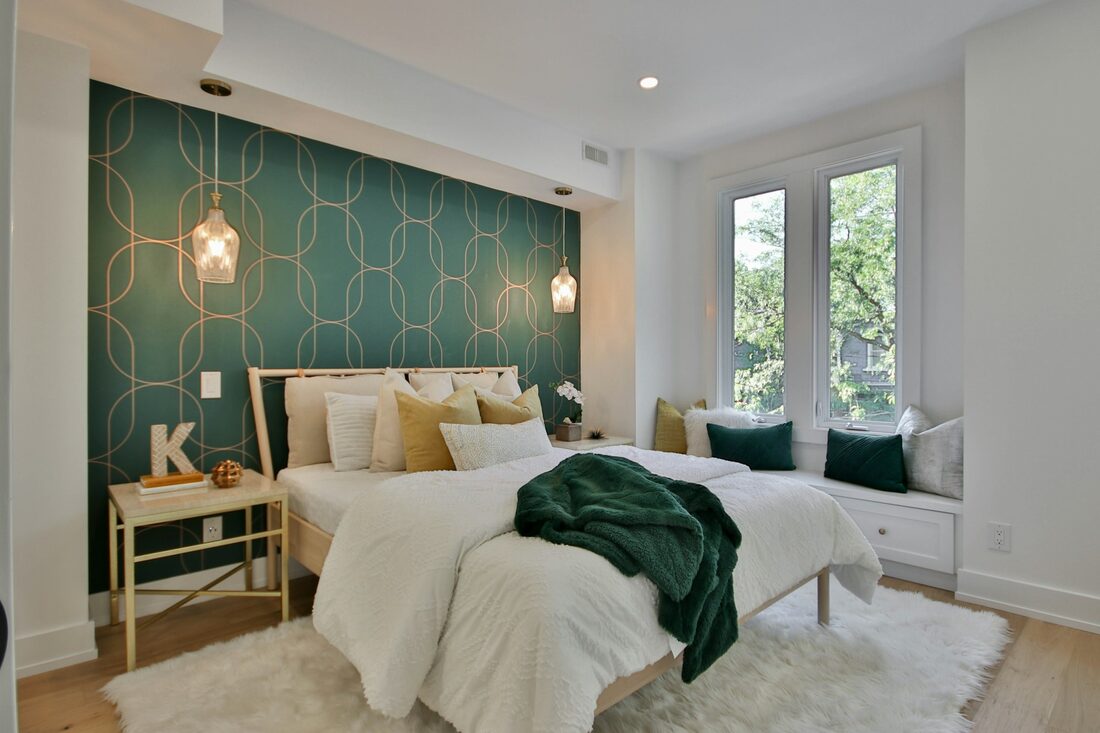 Bedroom with a teal geometric patterned wallpaper feature wall behind an upholstered bed