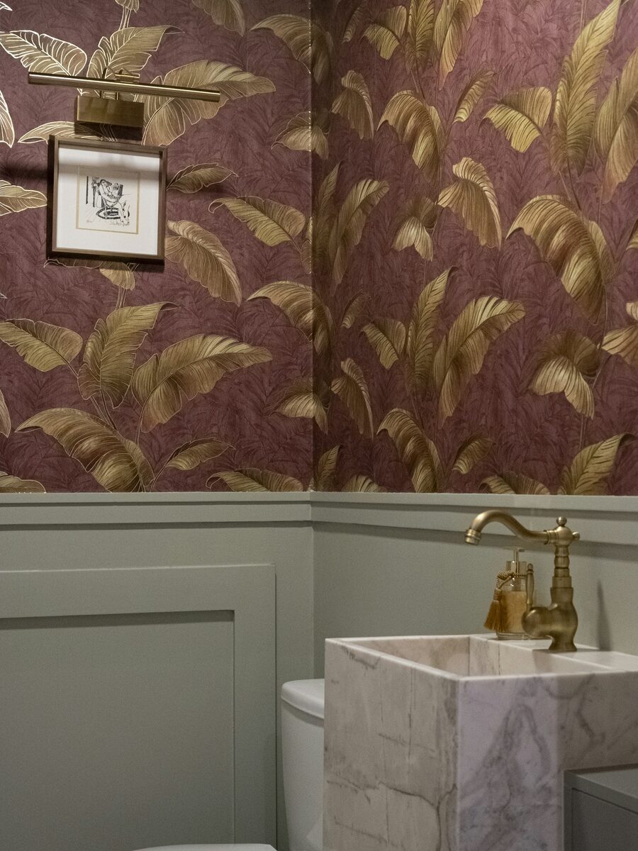 Powder room with a deep plum botanical wallpaper above white wainscoting and a stone vessel sink
