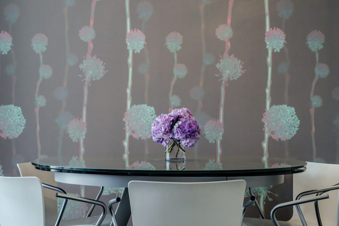 Dining room with a soft grey dandelion patterned wallpaper, a glass table and cream chairs