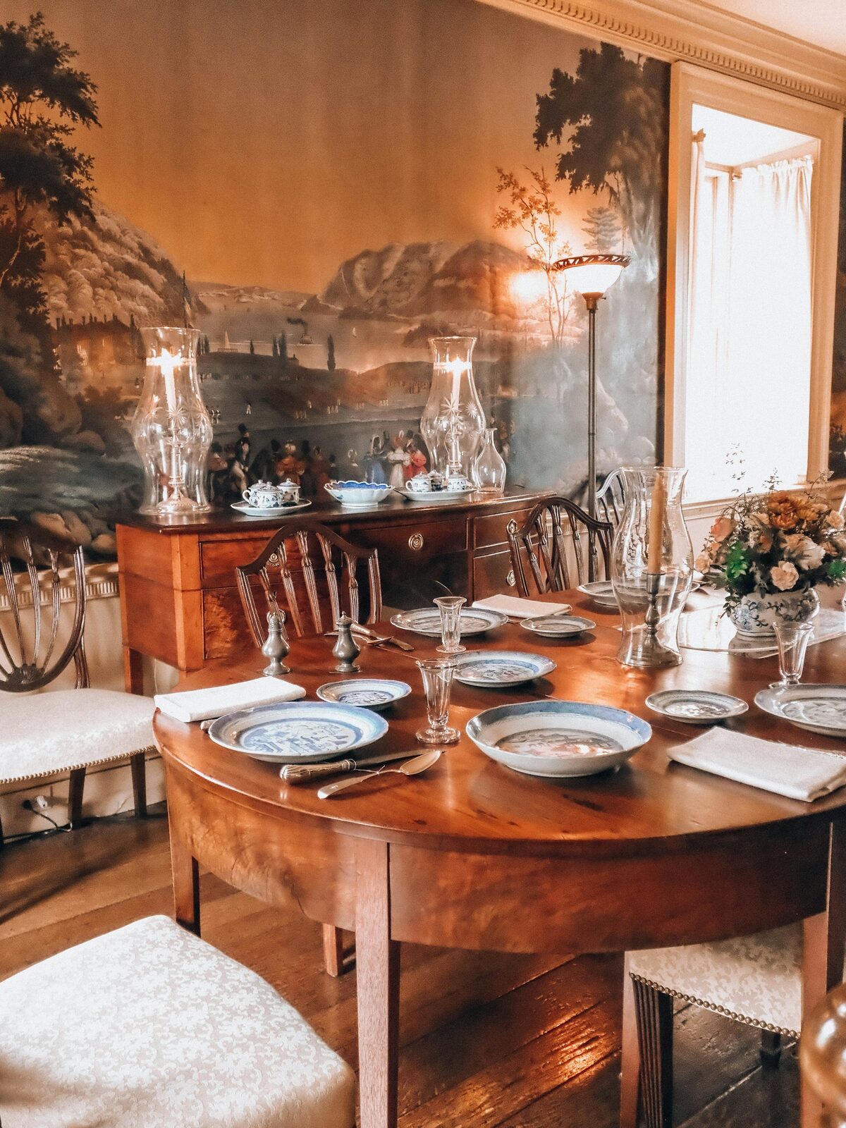 Elegant residential dining room with a scenic mural wallpaper covering the wall, a candle-lit table and warm lighting