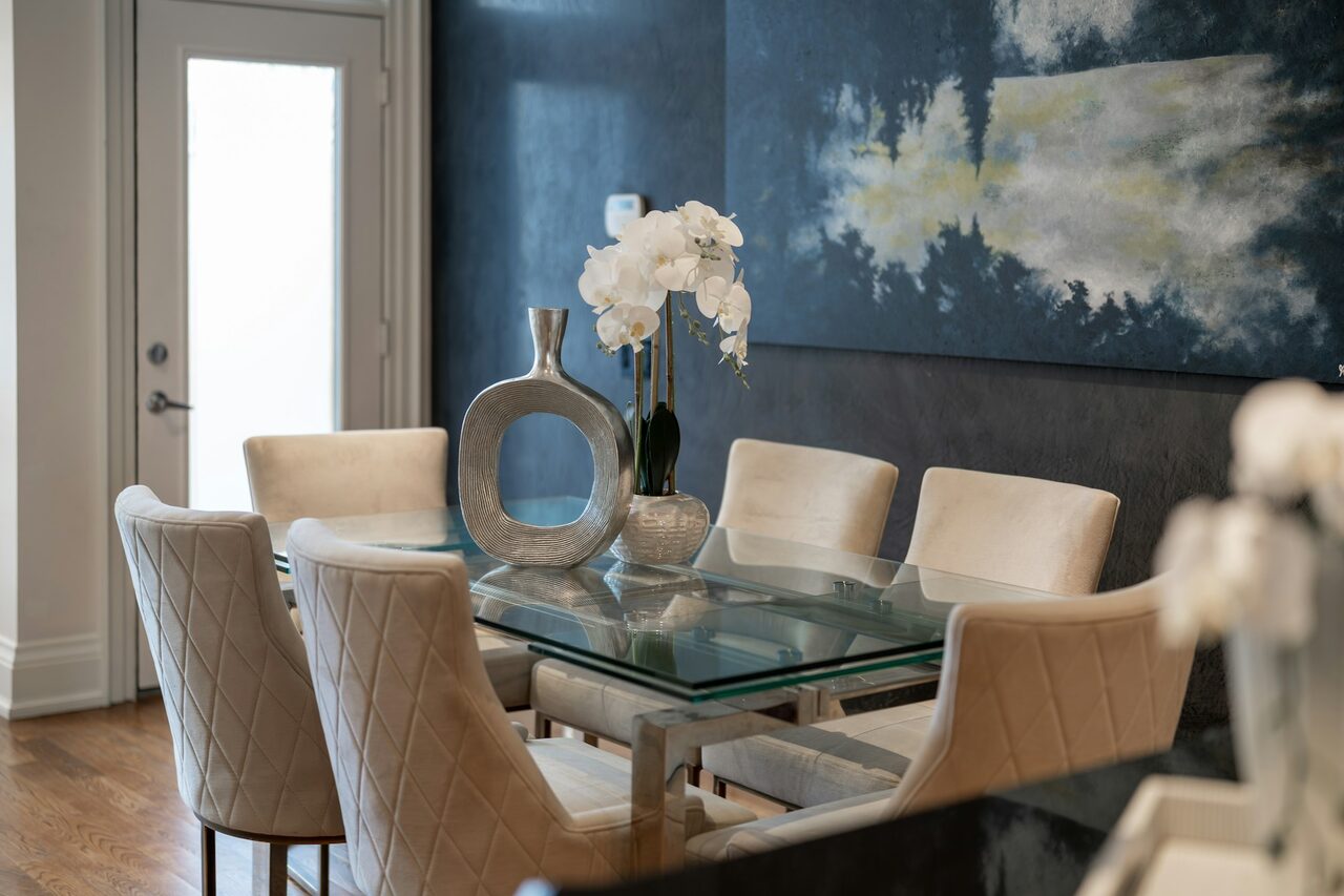Dining room with a deep blue scenic mural wallpaper, a glass table and a white orchid centerpiece